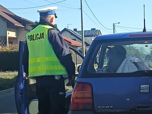 POLICJANT W KAMIZELCE ODBLASKOWEJ STOI PRZY SAMOCHODZIE W KTÓRYM SIEDZI KIEROWCA
