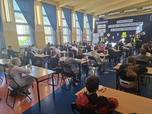 na dużej sali siedzą dzieci przy ławkach