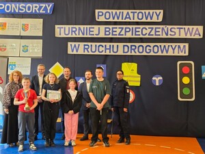na sali stoją dzieci trzymając dyplomy w rękach za ich plecaki stoi policjantka oraz dwaj mężczyźni i kobieta