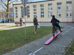 mężczyzna stoi i patrzy na dziecko jadące na  na rowerze po  kładce dziecko ma  kask na głowie