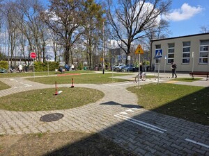 plac  obok szkoły miasteczko ruchu drogowego widoczny radiowóz i policjanci oraz dzieci z rowerami