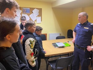 policjant stoi w pomieszczeniu na przeciwko młodzież widoczna tablica korkowa na niej zawieszone kartki