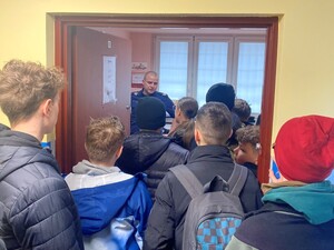 młodzież stoi w drzwiach do pomieszczenia w którym stoi policjant
