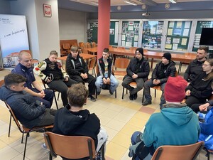 młodzież siedzi w kole na krzesłach na dużej sali wśród młodzieży siedzi policjant