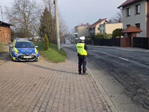 policjant z miernikiem stoi przy jezdni obok radiowóz