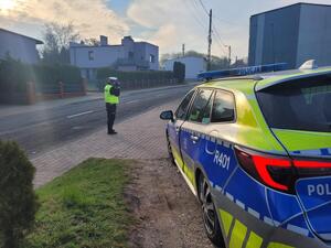 policjant stoi przy jezdni z miernikiem obok radiowóz