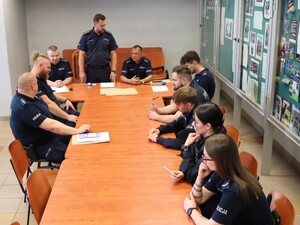 przy długim stole siedzą policjanci na końcu stołu stoi policjant