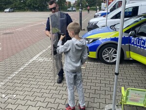 policjant i dziecko które trzyma tarcze policyjna w tle radiowóz