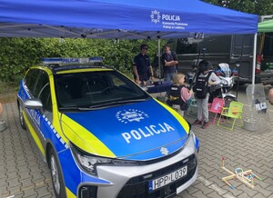 radiowóz dwoje dzieci policjant mężczyzna obok, dzieci oglądają kask i tarcze
