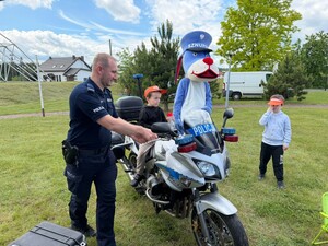 policjant motocykl na nim siedzi dziecko obok stoi dziecko i maskotka sznupka
