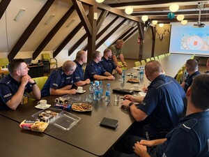 przy stole siedzą policjanci widoczny jest również ekran na którym wyświetlany jest slajd prezentacji obok stoi leśnik
