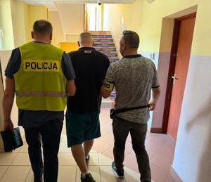 trzech mężczyzn idących korytarzem komendy jeden ma kamizelkę z napisem policja
