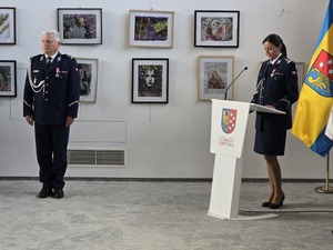 umundurowana policjantka stoi za mównica za nią widoczne są flagi obok stoi umundurowany policjant