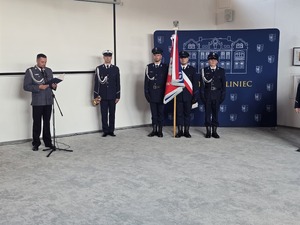 policjant stoi przed mikrofonem  obok stoi policjant z trąbka obok niego trzech policjantów ze sztandarem