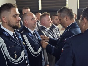 umundurowani policjanci stoja w rzędzie jeden policjant przypina policjantowi medal