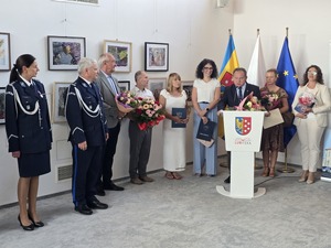 dwoje umundurowanych policjantów obok nich stoją ludzie w cywilnych ubraniach jeden z nich stoi za mównicą