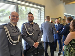 dwóch policjantów stoi obok siebie z boku widoczna kobieta ubrana w sukienkę