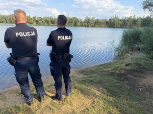 Umundurowani policjanci na tle zbiornika wodnego.